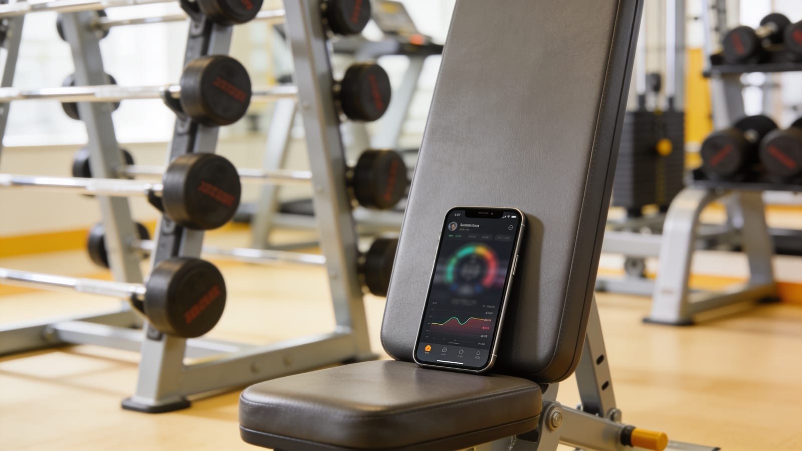 Salle de sport moderne avec machines de musculation et haltères, smartphone posé sur un banc affichant une app de fitness